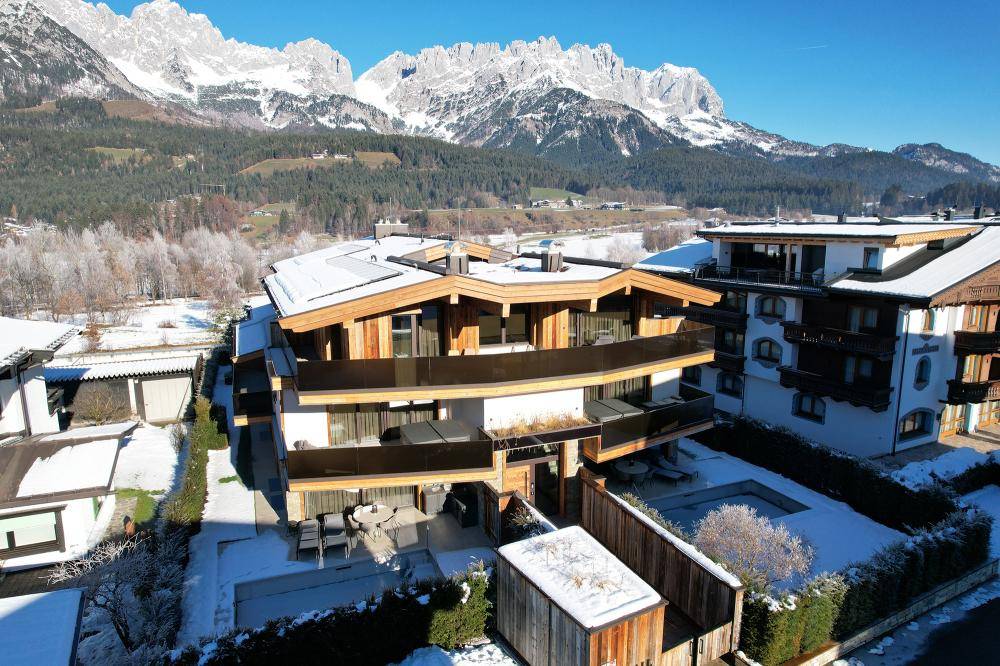 Gesamtanblick des modernen Wohngebäudes mit umliegenden Gärten und verschneiter Landschaft im Winter.