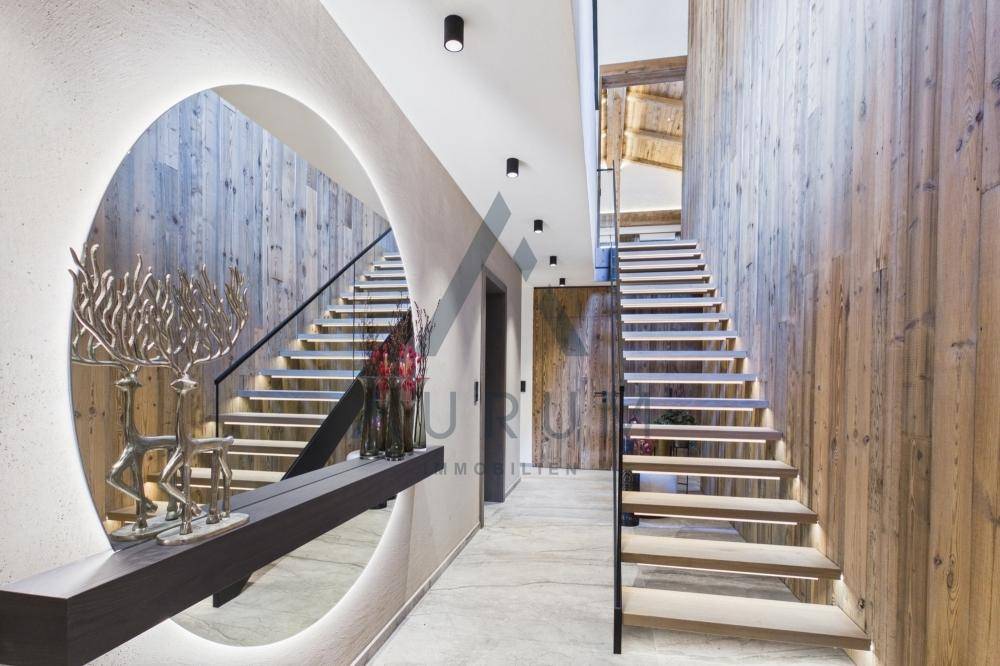 Heller Flur mit Holzvertäfelung, moderner Treppe und dekorativem Spiegel.