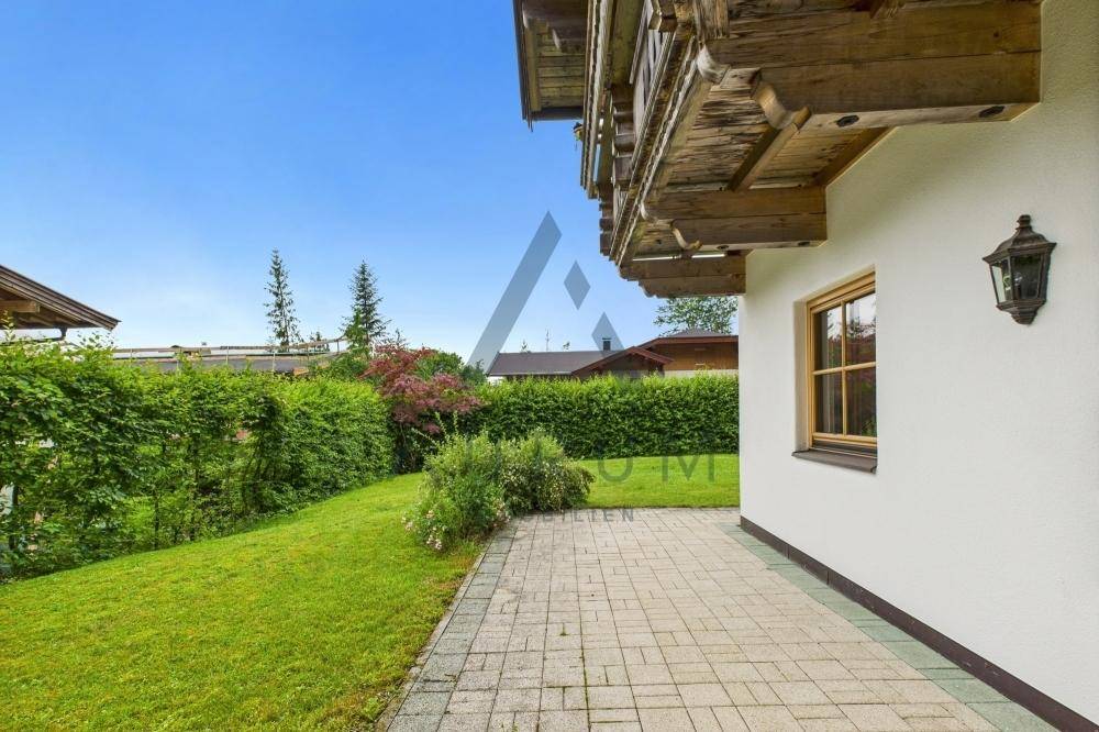 Gepflasterte Terrasse neben einem gepflegten Rasenbereich mit Hecke und Blick auf die Umgebung.
