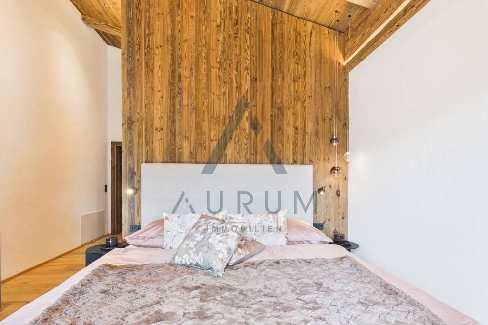 Gemütliches Schlafzimmer mit Holzwand, Holzbalkendecke und weichem Teppichboden.