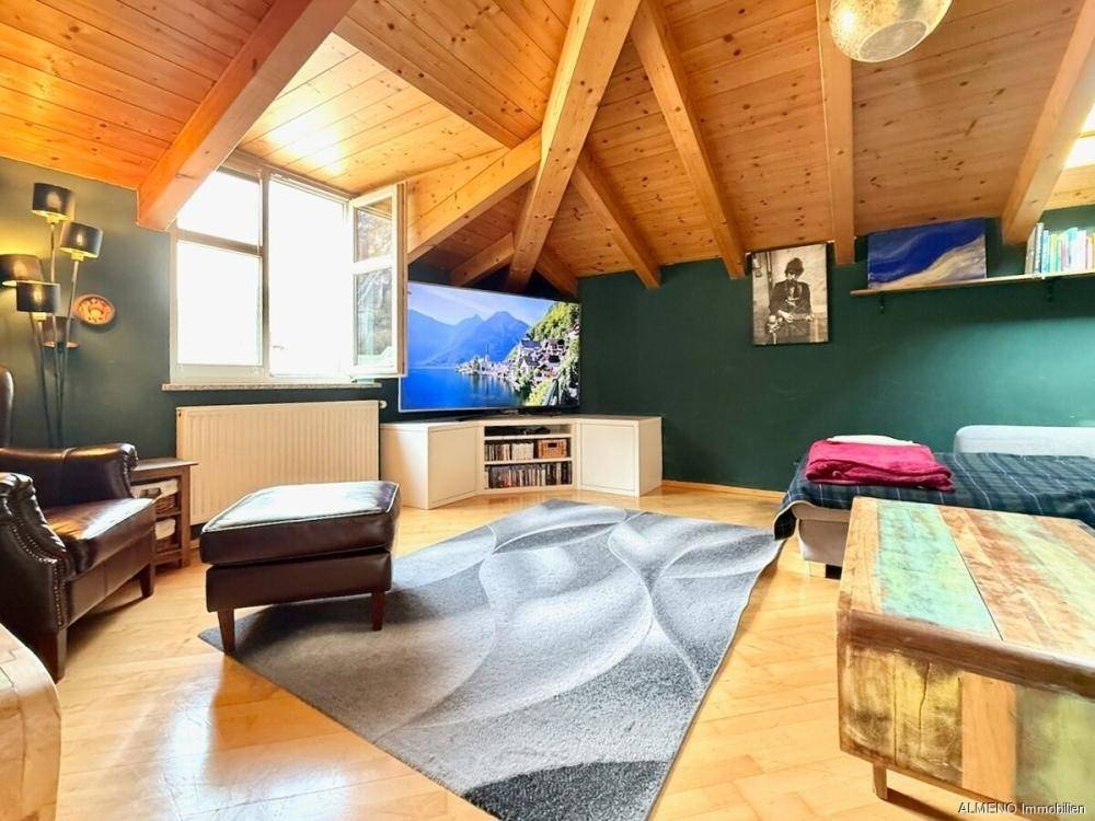 Helles Wohnzimmer im Dachgeschoss mit sichtbaren Holzbalken, schrägen Wänden und Holzboden.