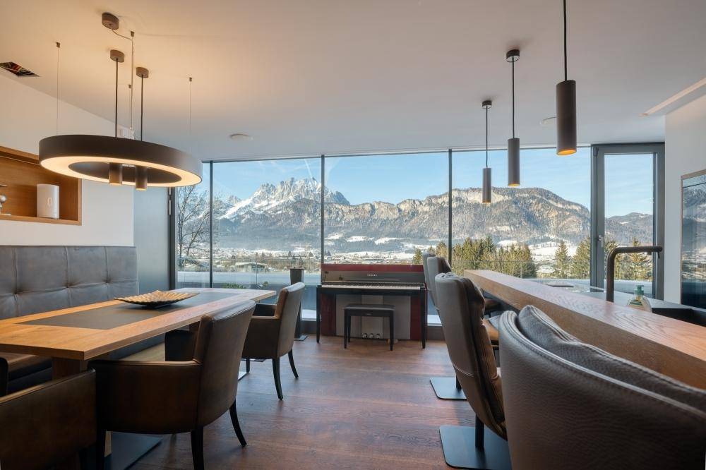 Eleganter Essbereich mit Klavier und raumhohen Fenstern, die einen weiten Bergblick bieten.
