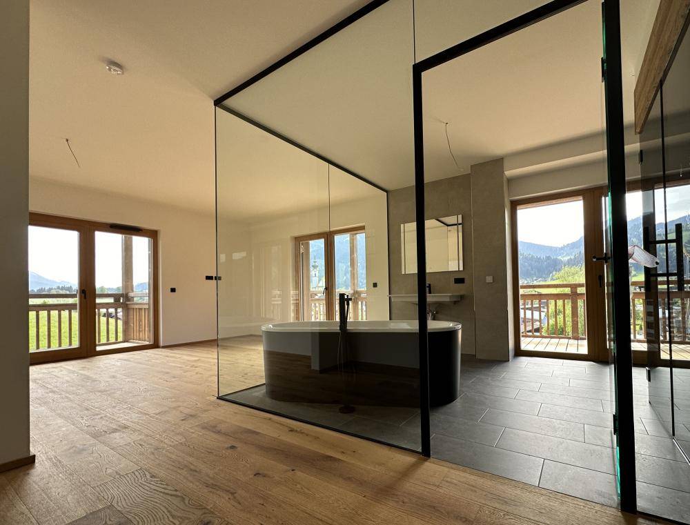 Geräumiges Badezimmer mit freistehender Badewanne, Holzboden und großen Fenstern mit Bergblick.