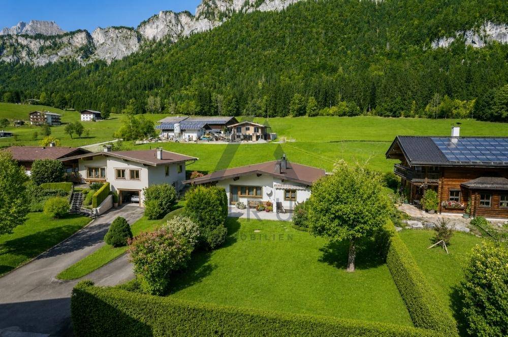 Panoramablick auf ein Haus mit Garten, umgeben von grünen Wiesen und majestätischen Bergen.