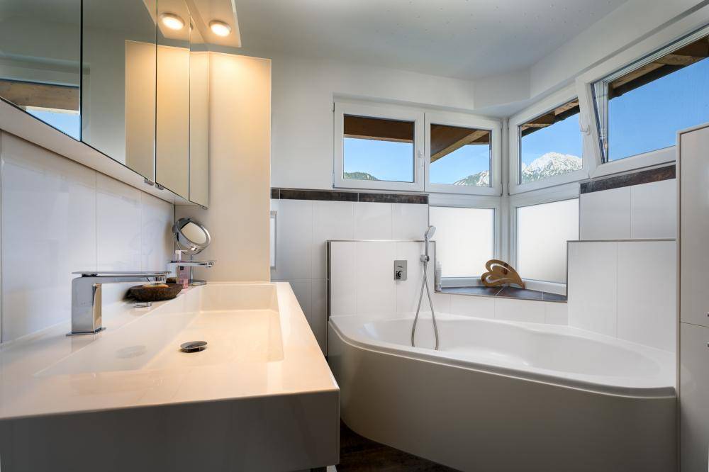Helles Badezimmer mit Eckbadewanne, modernem Waschtisch und Fenstern mit Bergblick.