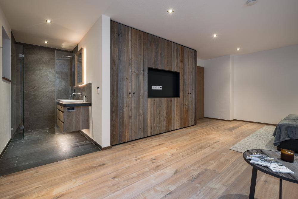 Schlafzimmer mit Holzwand, integriertem Fernseher und offenem Zugang zum modernen Bad.