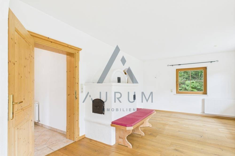 Gemütlicher Wohnraum mit traditionellem Kachelofen, Holzboden und Blick ins Grüne.