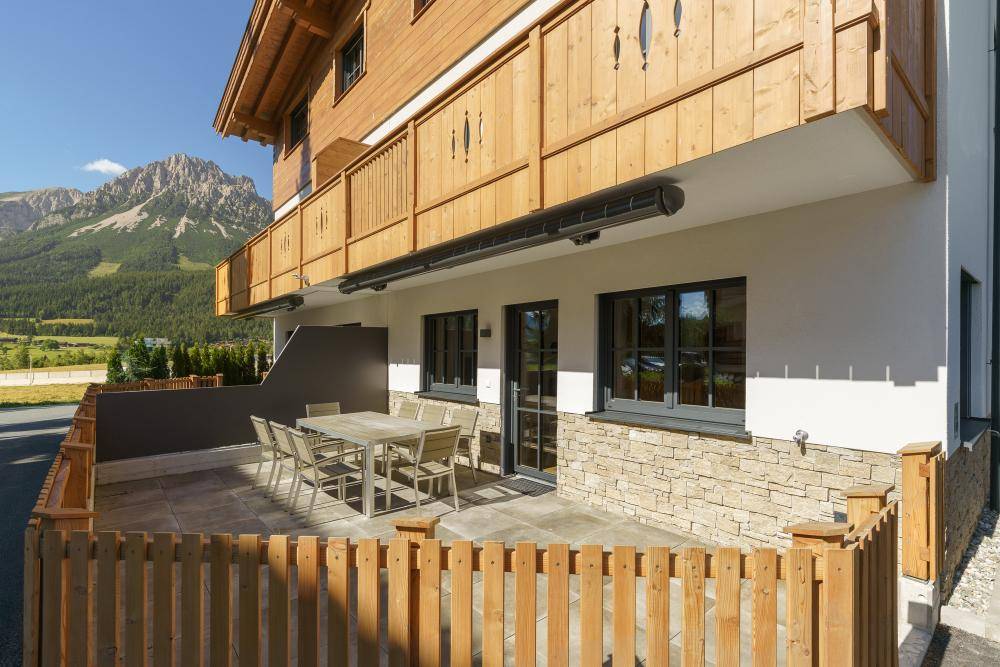 Geräumige Terrasse im Erdgeschoss mit Esstisch und Stühlen, umgeben von einer Holzumzäunung und Bergblick.