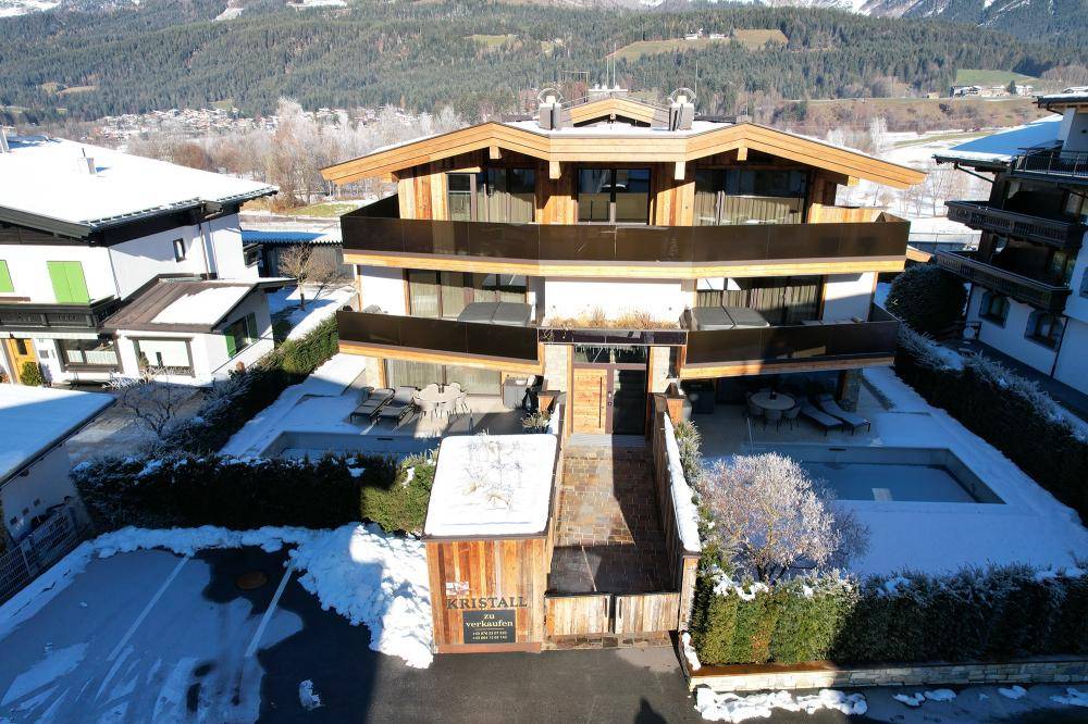 Panoramablick auf das moderne Wohnhaus mit Eingangsbereich, Parkplätzen und verschneiten Außenanlagen.