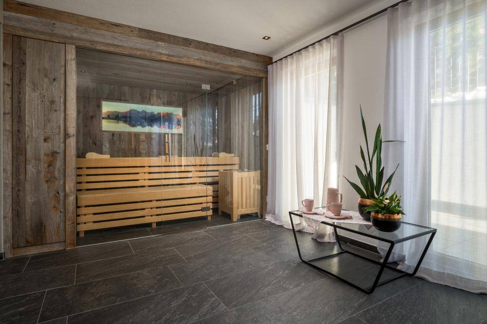 Entspannungsbereich mit moderner Sauna, großen Fenstern und dunklem Fliesenboden.