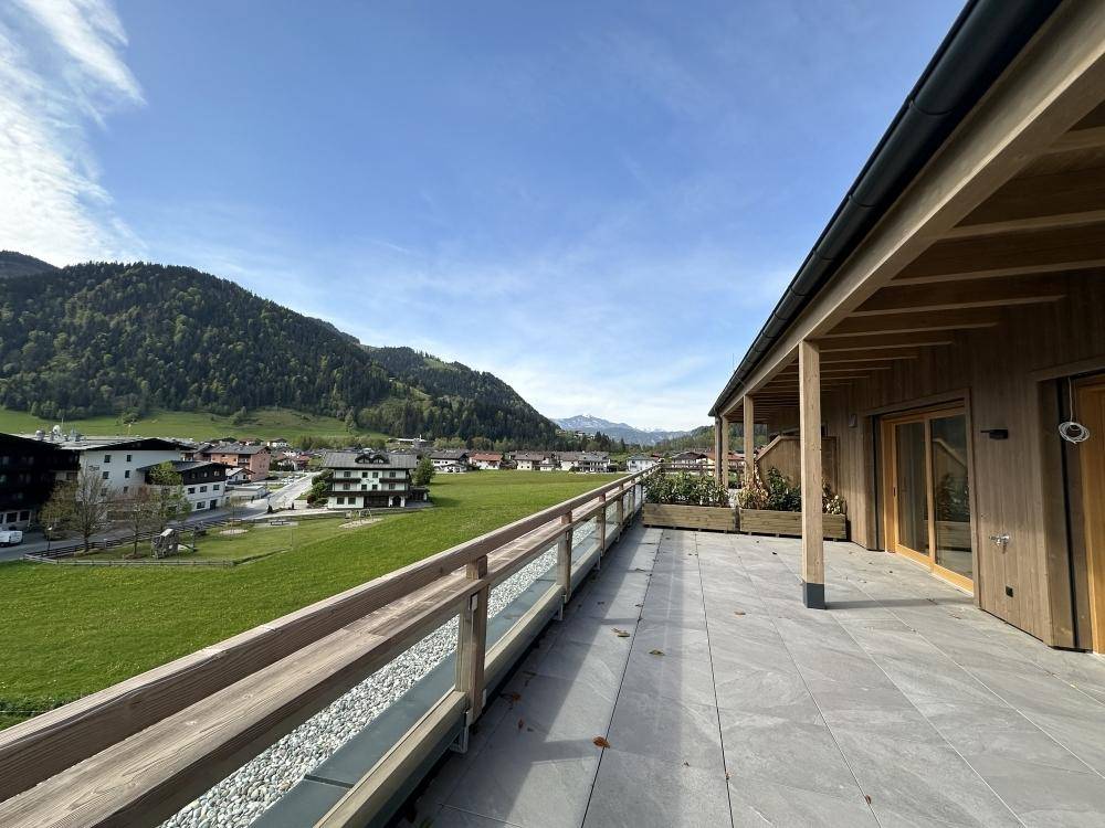 Weitläufige Terrasse mit Fliesenboden und Holzgeländer, bietet einen schönen Blick auf die grüne Landschaft und das Dorf.