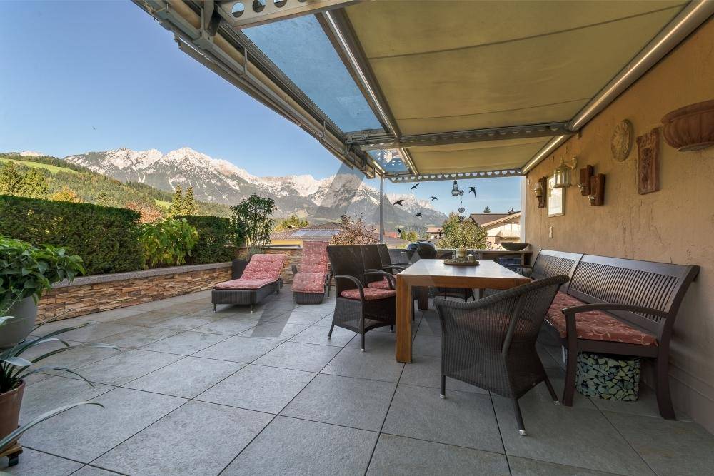 Geräumige Terrasse mit Fliesenboden, Essbereich und Liegestühlen, umgeben von einer Hecke mit Bergblick.