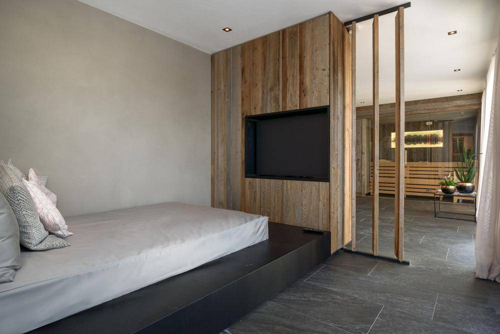 Schlafzimmer mit Bettplattform, Holzwand und Blick auf den angrenzenden Wellnessbereich.
