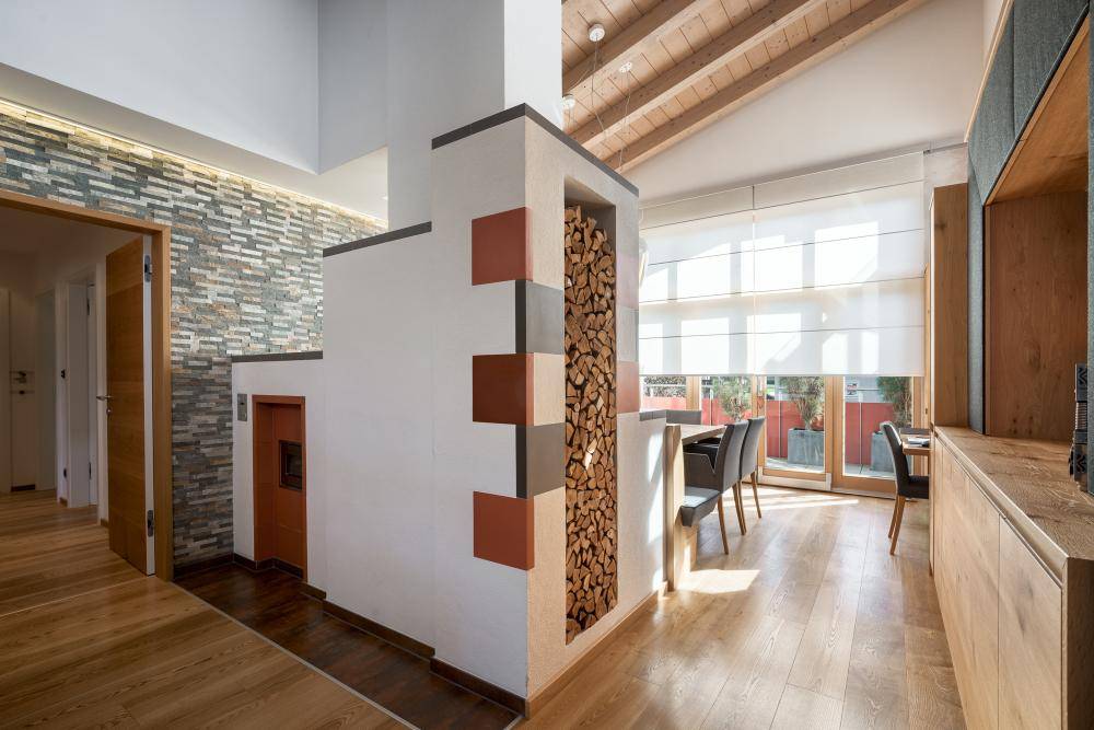 Gemütlicher Essbereich mit Holzboden, großen Fenstern und einem dekorativen Kachelofen mit Holzfach.