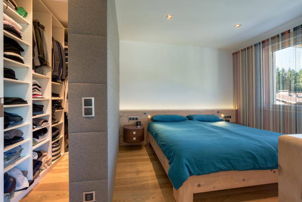 Schlafzimmer mit Holzboden, modernem Bett und offenem Zugang zu einem begehbaren Kleiderschrank.