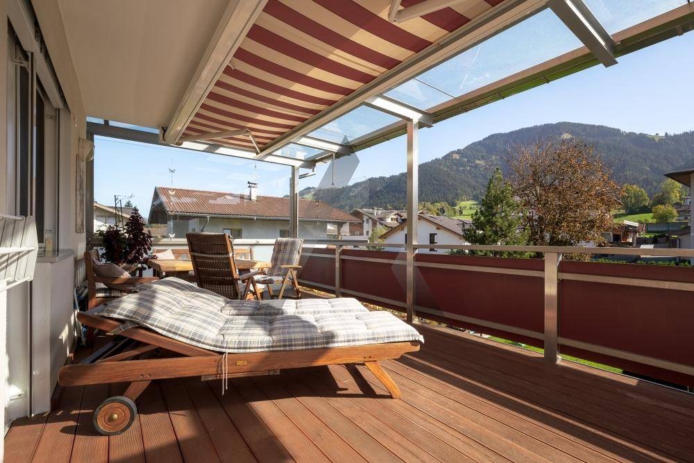 Sonniger Balkon mit Holzdeck, Liegestuhl und Markise, ideal zum Entspannen mit Blick auf die grüne Umgebung.