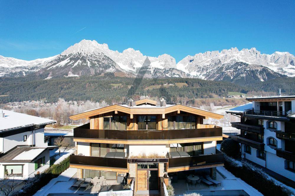 Architektonisch ansprechendes Gebäude mit Holzfassade und großen Glasflächen vor winterlicher Bergkulisse.