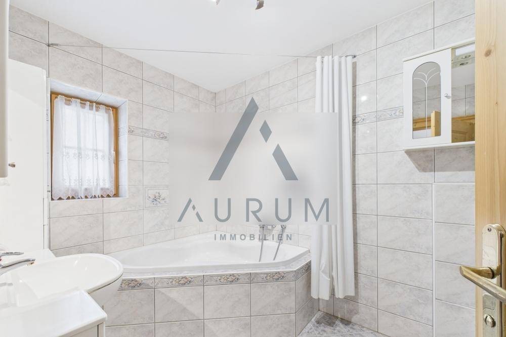 Gefliestes Badezimmer mit Eckbadewanne, Duschvorhang und Fenster für Tageslicht.