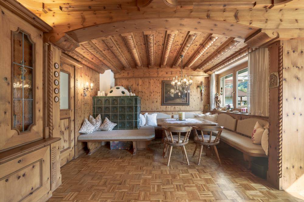 Rustikaler Essbereich mit umfassender Holzvertäfelung, Holzbalkendecke und einem grünen Kachelofen.