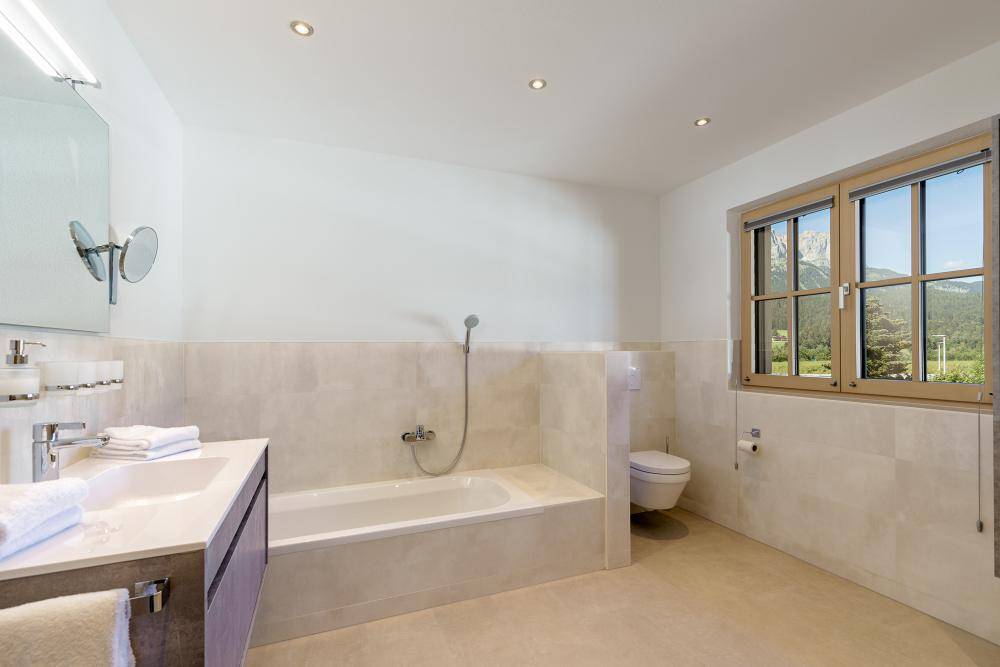 Modernes Badezimmer mit Badewanne, Waschtisch und Fenster mit Blick auf die Berge.