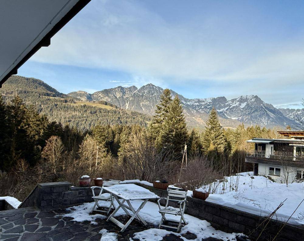 Verschneite Terrasse mit Gartenmöbeln und beeindruckendem Panoramablick auf die Berge.