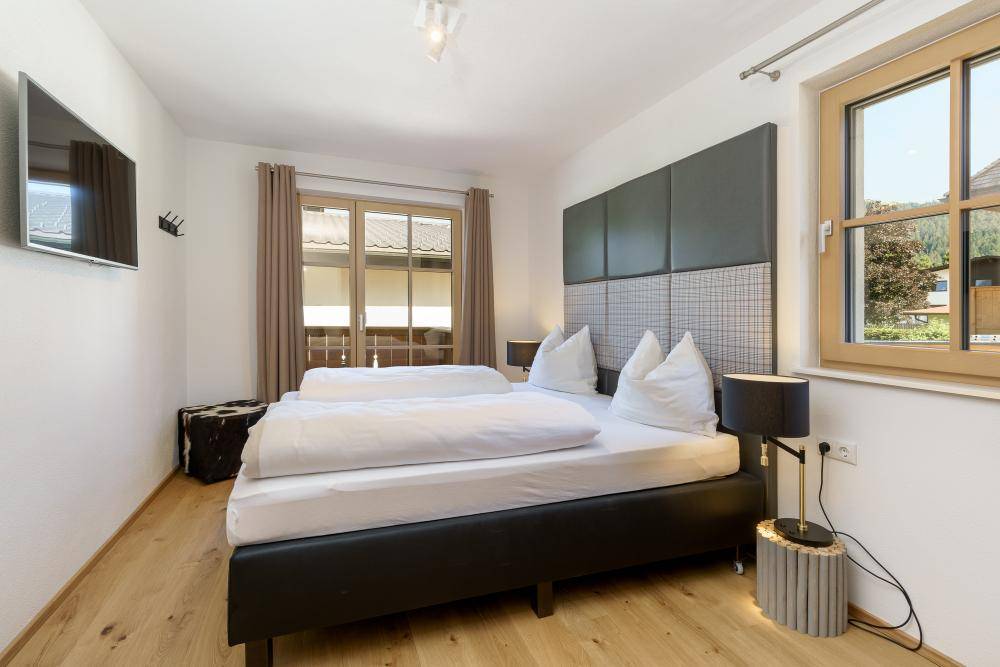 Komfortables Schlafzimmer mit Doppelbett, Holzboden und zwei Fenstern für viel Tageslicht.