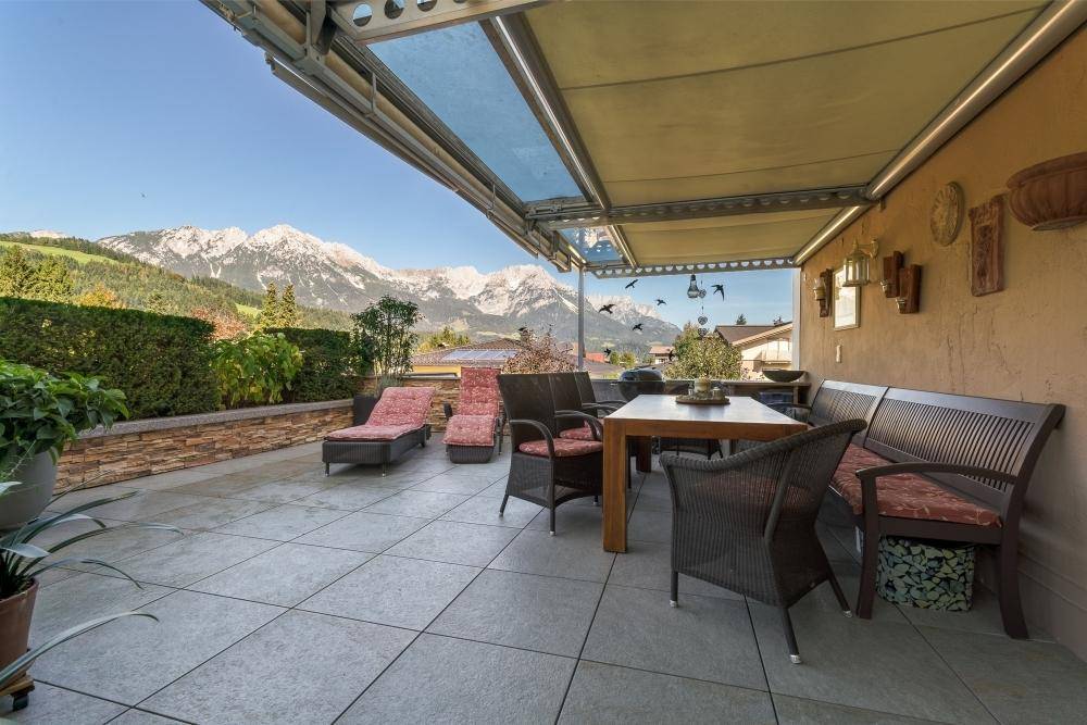 Geräumige Terrasse mit Fliesenboden, Essbereich und Liegestühlen, umgeben von einer Hecke mit Bergblick.