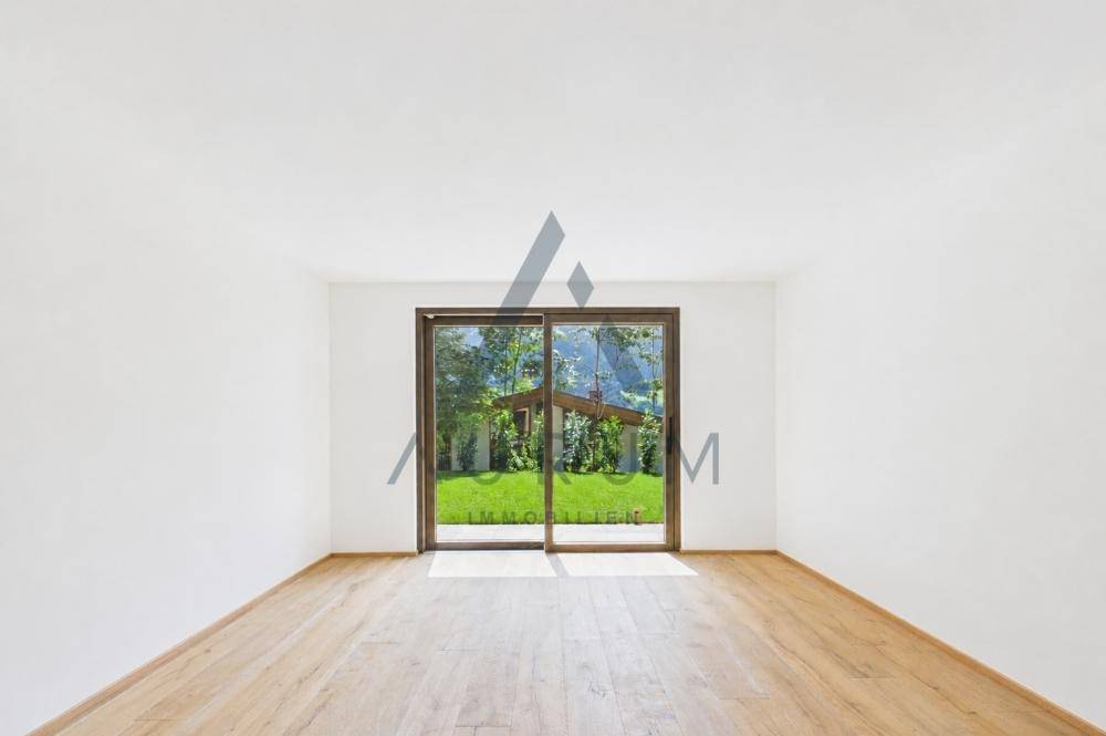 Leerer Raum mit Holzboden und großer Glasschiebetür zum Garten.