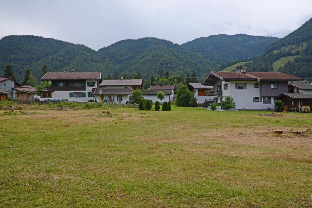 Grüne Wiese mit Blick auf eine Reihe von Wohnhäusern und die umliegende Berglandschaft.