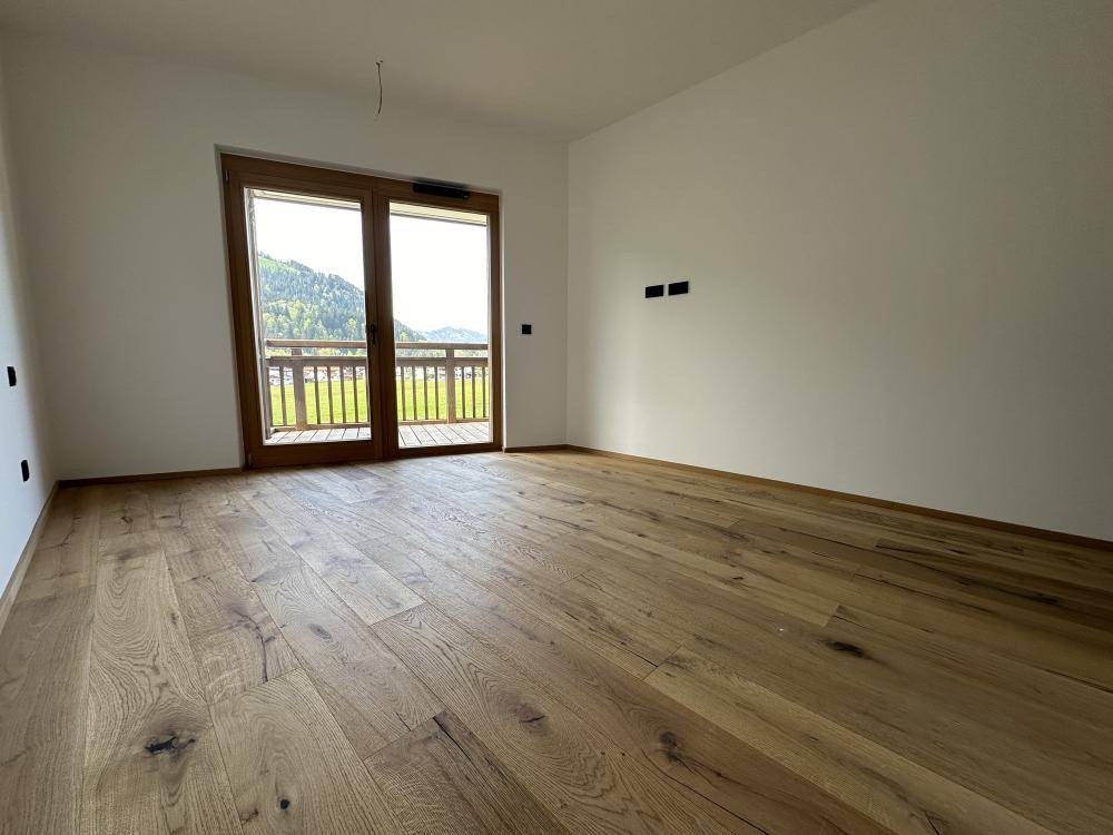 Helles Zimmer mit Holzboden und Zugang zu einem Balkon mit Bergblick.