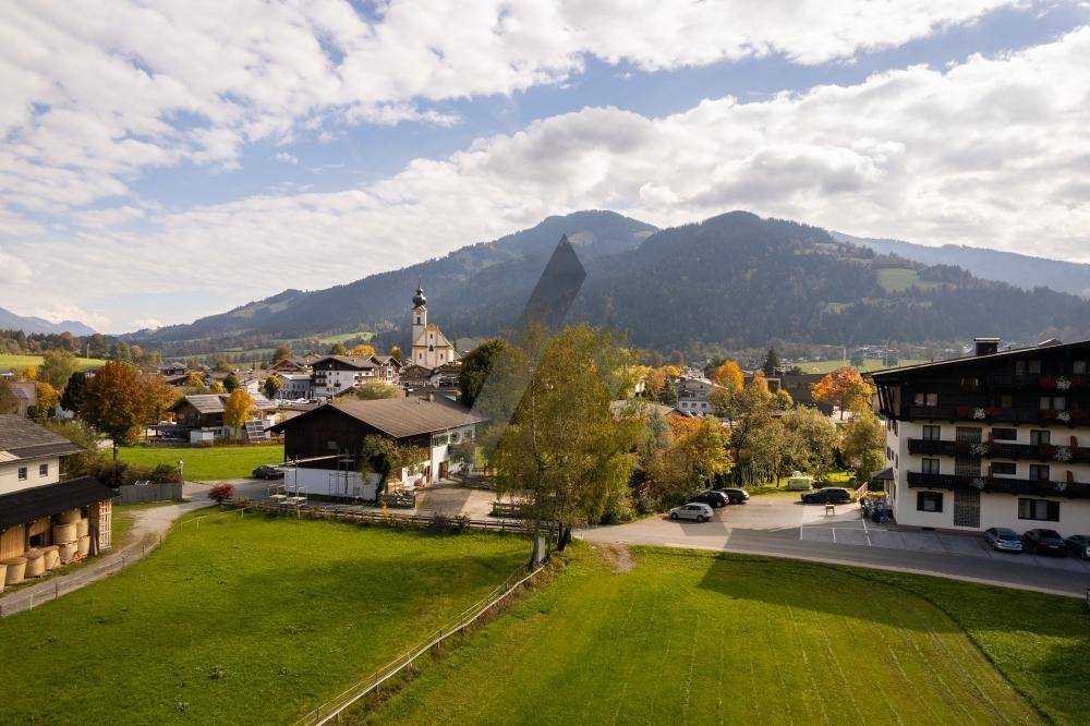 Panoramablick auf ein charmantes Dorf mit Kirche und umliegenden Bergen unter einem weiten Himmel.