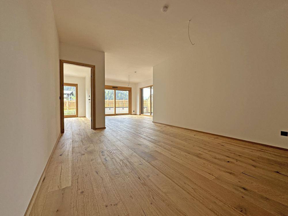 Geräumiger, heller Wohnbereich mit Holzboden und mehreren Zugängen zu Außenbereichen.