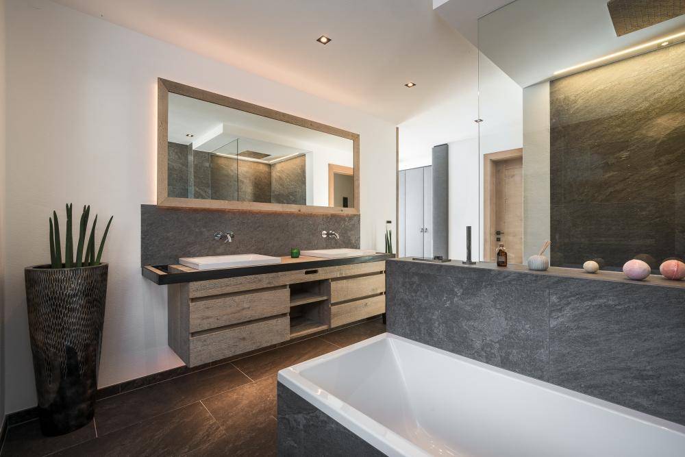 Modernes Badezimmer mit Doppelwaschbecken, großer Badewanne und dunklen Steinfliesen.
