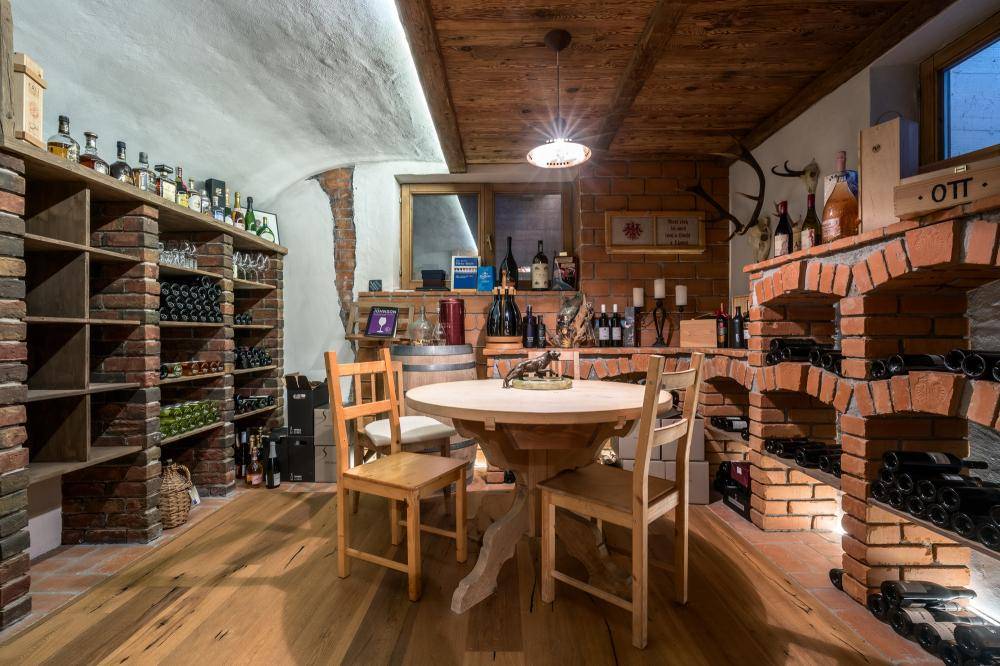 Rustikaler Weinkeller mit Ziegelwänden, Holzregalen und einem gemütlichen Verkostungsbereich.