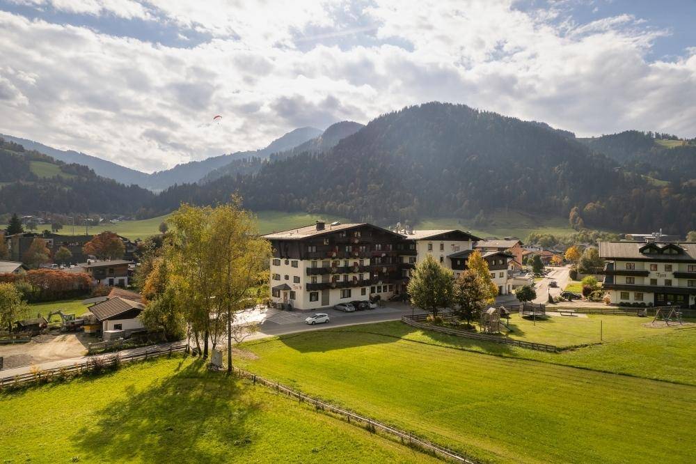 Luftaufnahme eines traditionellen Gebäudes mit Balkonen, eingebettet in eine grüne Landschaft mit Bergen im Hintergrund.