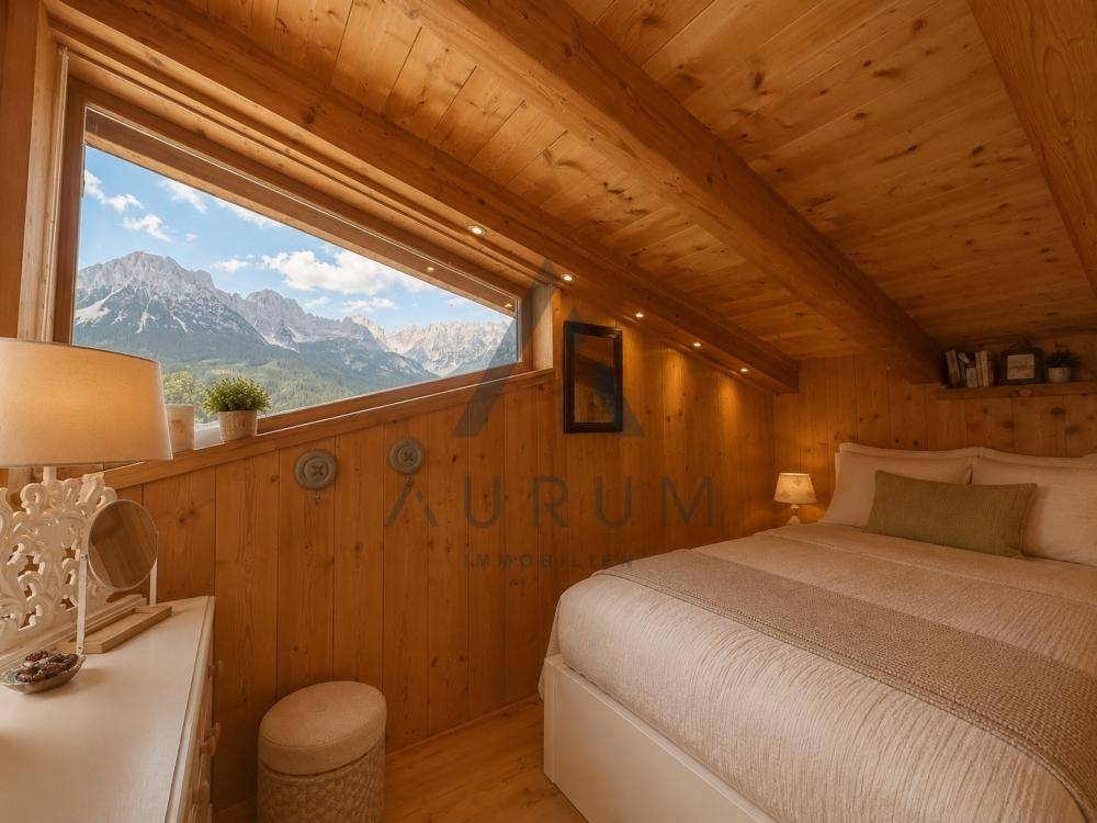 Gemütliches Schlafzimmer im Dachgeschoss mit Holzverkleidung und breitem Fenster mit Bergblick.