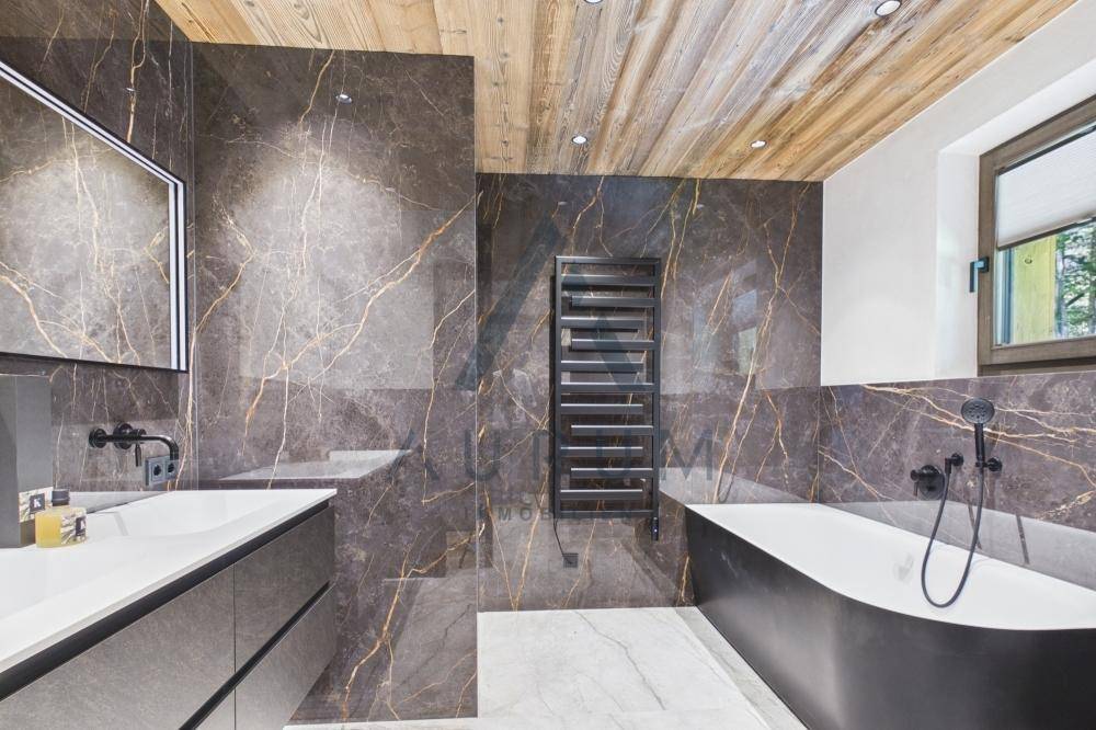 Elegantes Badezimmer mit dunklen Marmorfliesen, freistehender Badewanne und Fenster.
