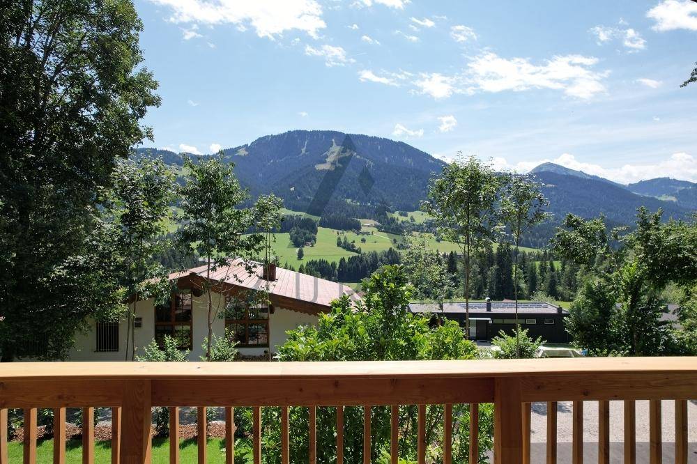 Panoramablick von der Terrasse auf die grüne Berglandschaft und umliegende Häuser.