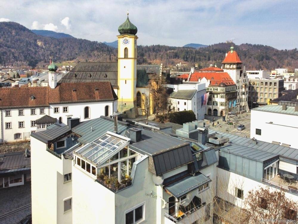 Panoramablick über die Dächer der Stadt mit historischer Kirche und umliegender Berglandschaft.