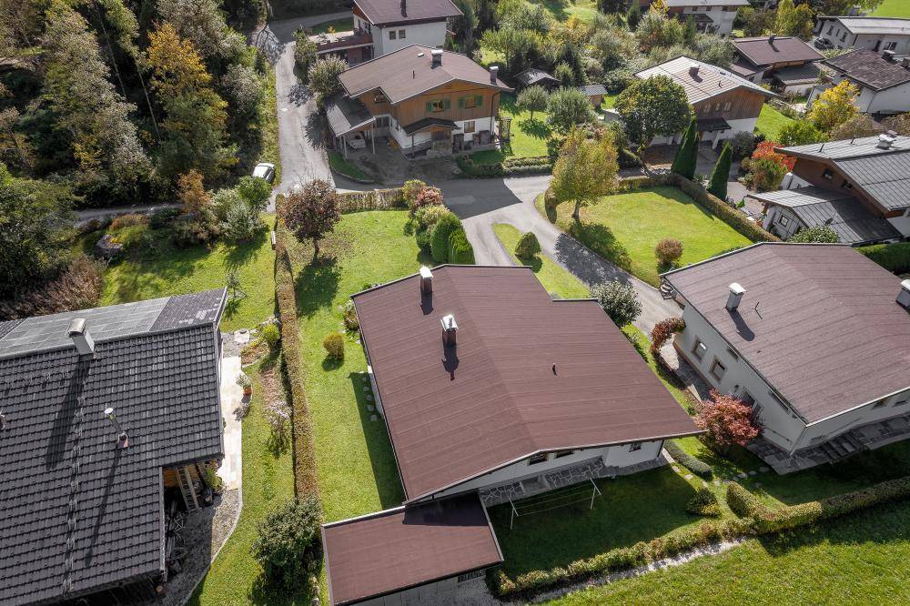 Dachansicht eines Hauses mit dunklem Ziegeldach, umgeben von grünen Gärten und einer Zufahrt.