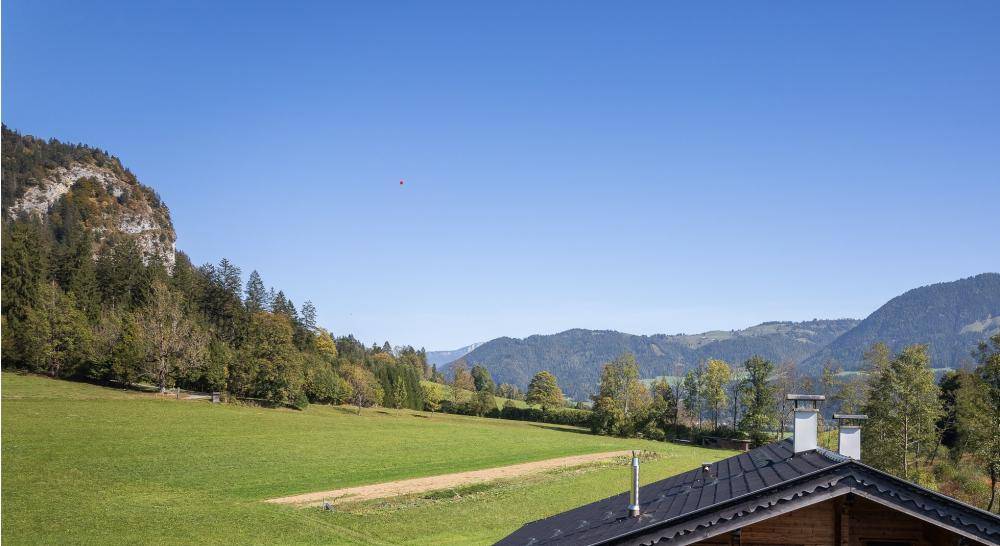 Weitläufiger Blick über grüne Wiesen und bewaldete Hügel unter einem klaren, blauen Himmel.