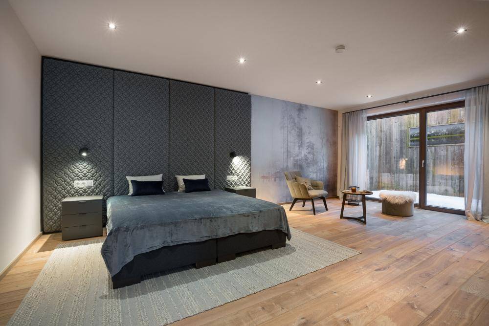 Geräumiges Schlafzimmer mit Holzboden, gepolsterter Wand und Zugang zu einem Außenbereich.
