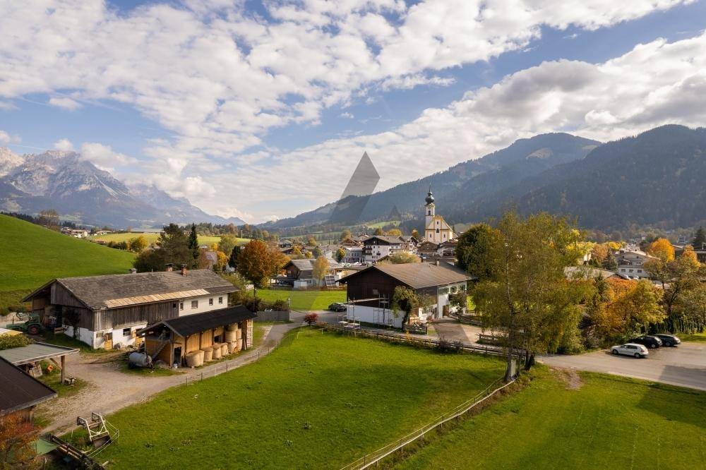 Idyllisches Dorf mit traditionellen Häusern und einer Kirche, eingebettet in eine grüne Berglandschaft.