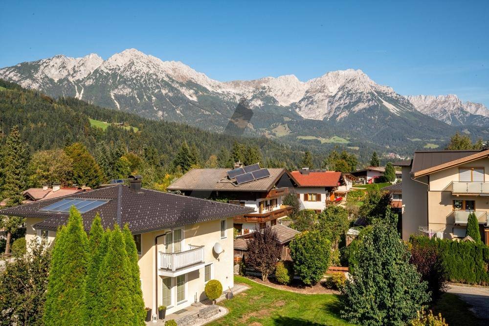 Panoramablick auf eine Wohnsiedlung mit traditionellen Häusern und majestätischen Bergen im Hintergrund.