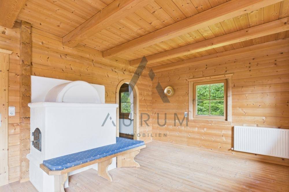 Rustikaler Wohnraum mit Holzwänden, Kachelofen und einer gemütlichen Sitzbank am Fenster.