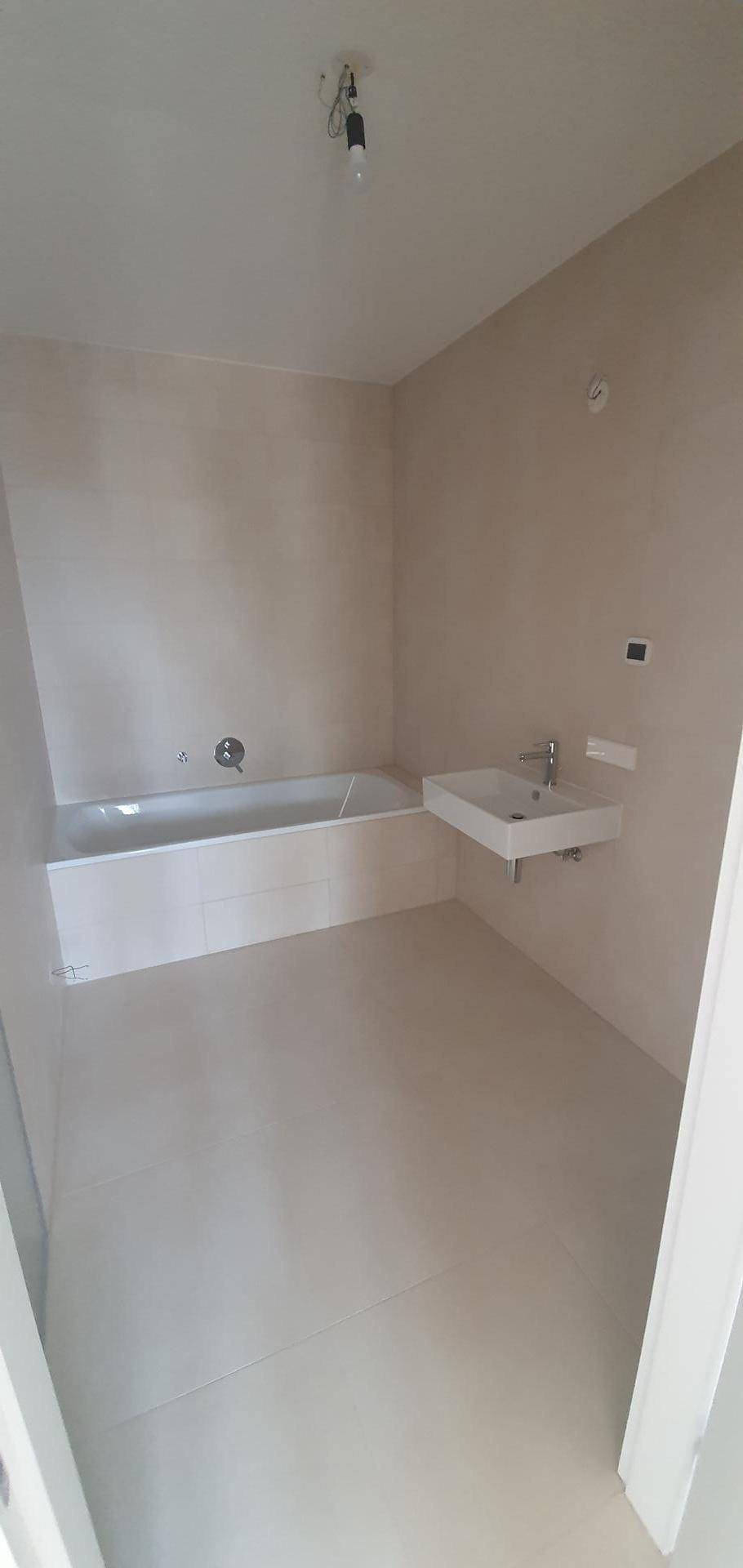 Modernes Badezimmer mit Badewanne und Einzelwaschbecken, ausgestattet mit hellen Fliesen.