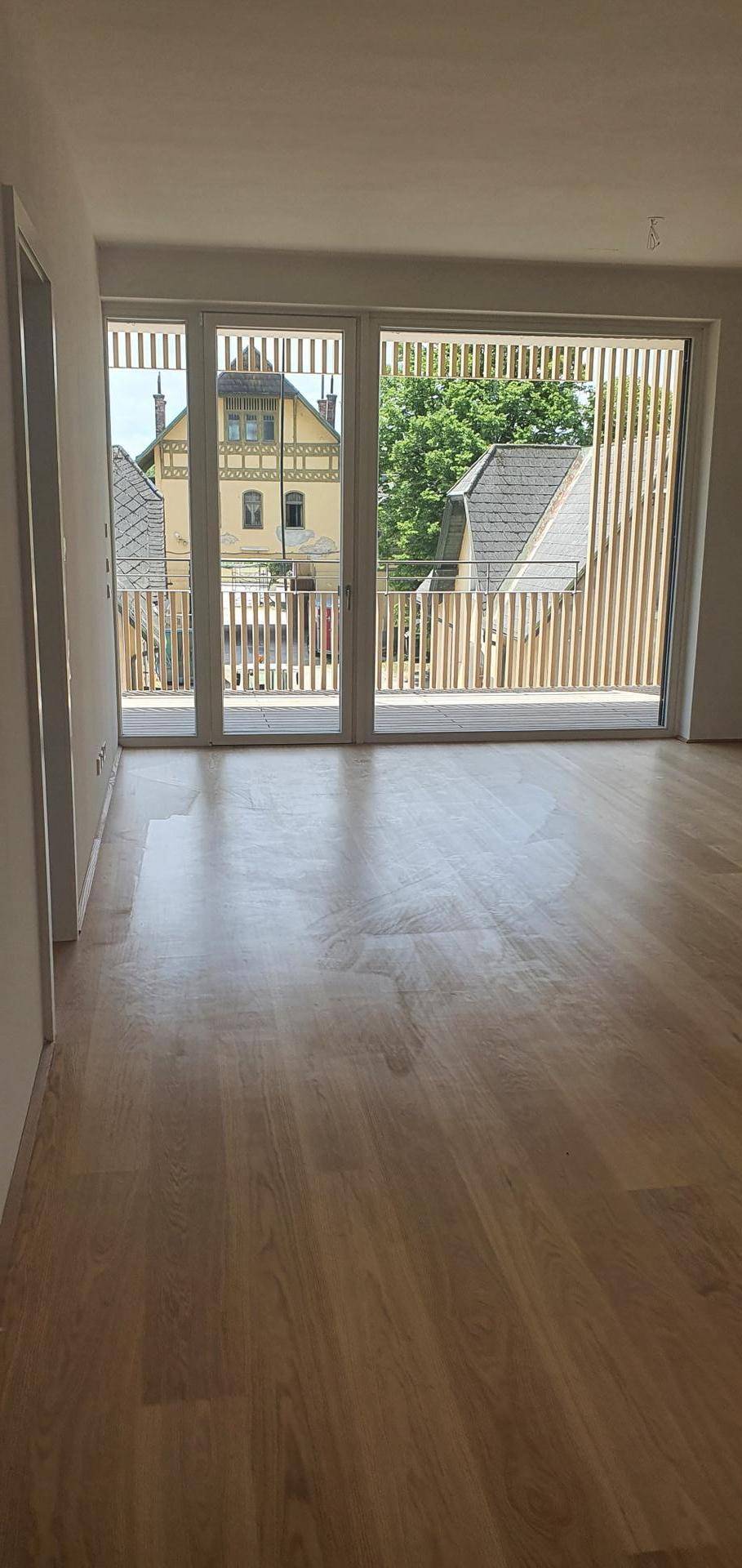 Lichtdurchfluteter Raum mit elegantem Holzboden und breiter Fensterfront zum Balkon.