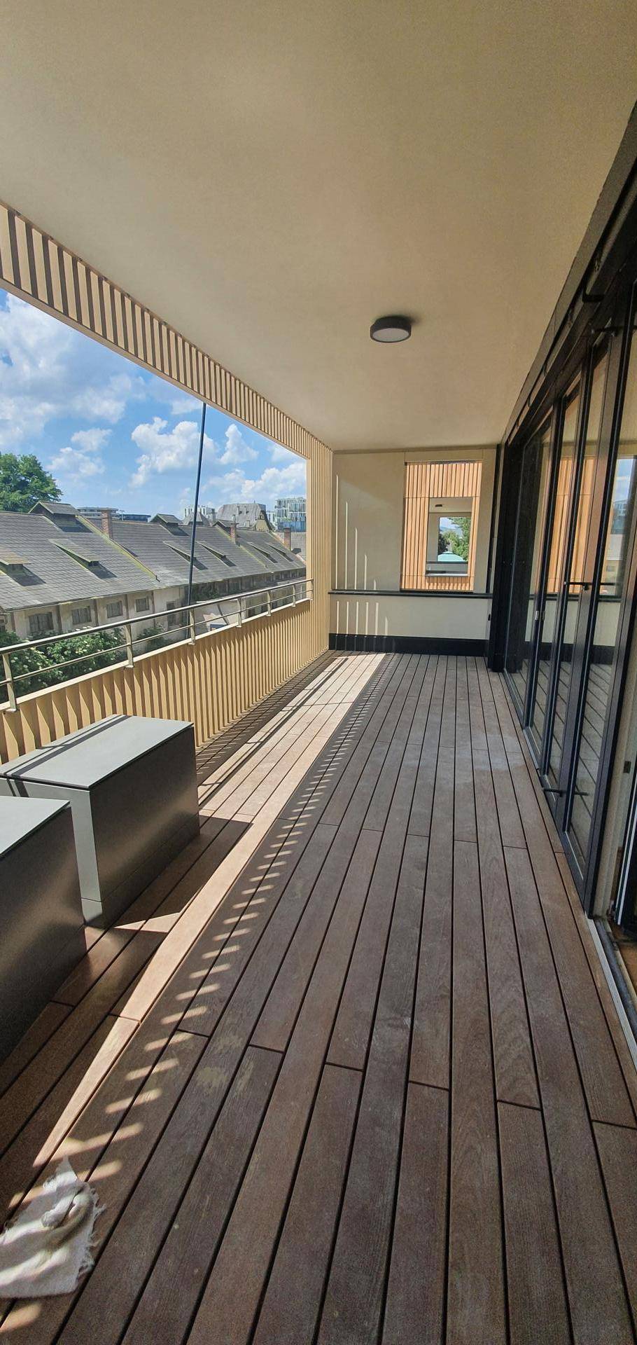 Geräumiger Balkon mit Holzbelag und Blick über die Dächer sowie ins Grüne.