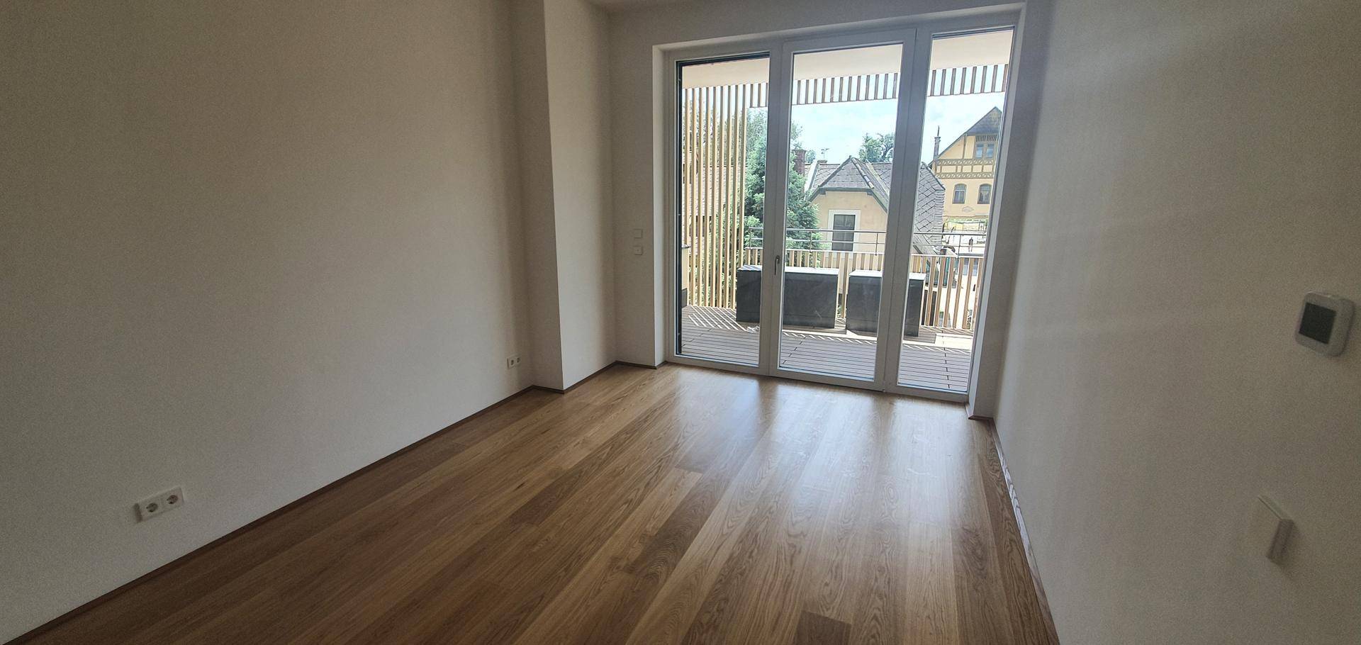 Geräumiges Schlafzimmer mit Holzboden und großen Fenstern, die viel Tageslicht hereinlassen.
