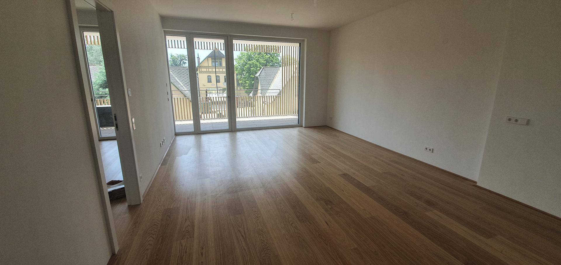 Großzügiger Wohnbereich mit Holzboden und Zugang zu einem sonnigen Balkon.